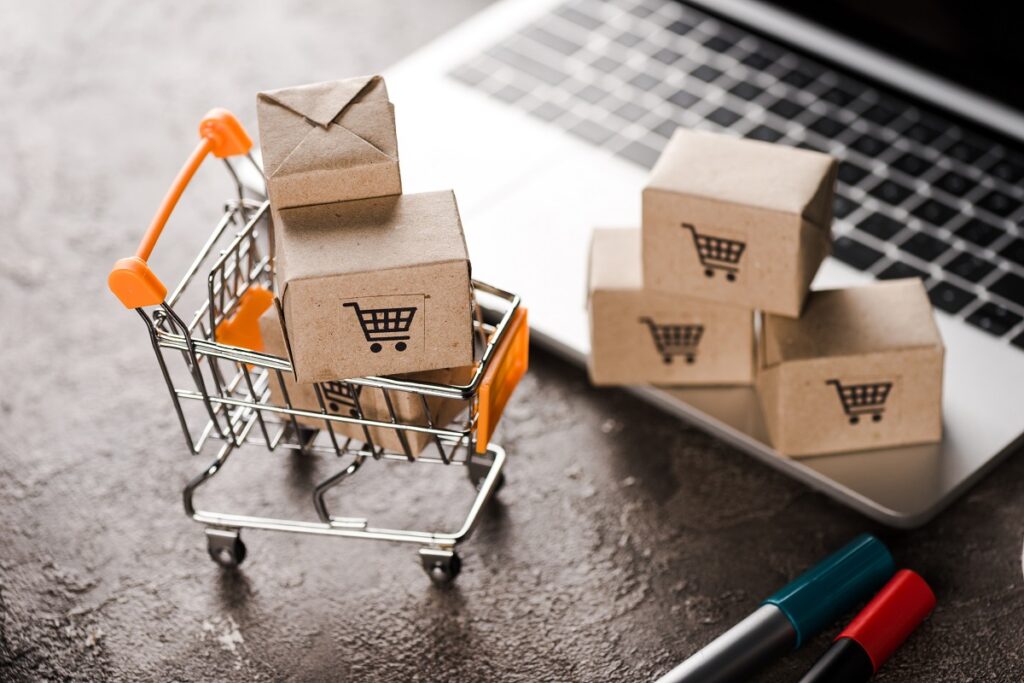 concept image of ecommerce featuring small cart with boxes, above a laptop