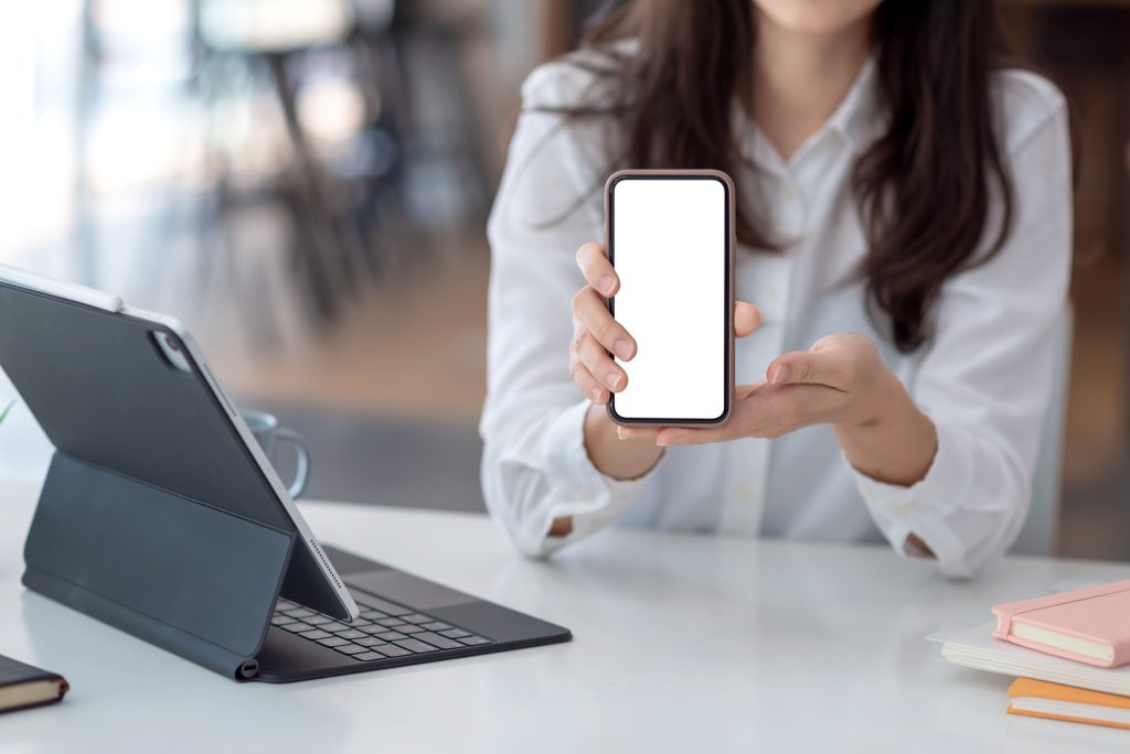 Close-up of a woman hand holding mobile phone white blank screen at the office.