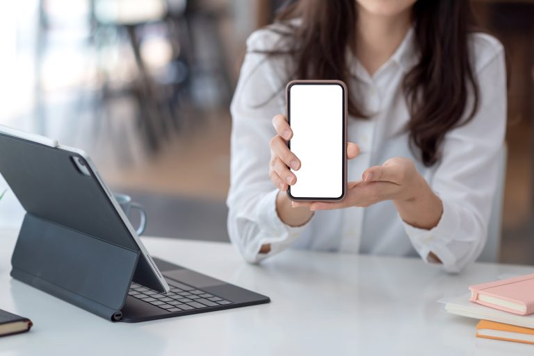 Close-up of a woman hand holding mobile phone white blank screen at the office.